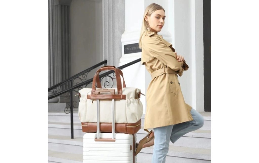 A woman in trench coat and jeans with luggage.