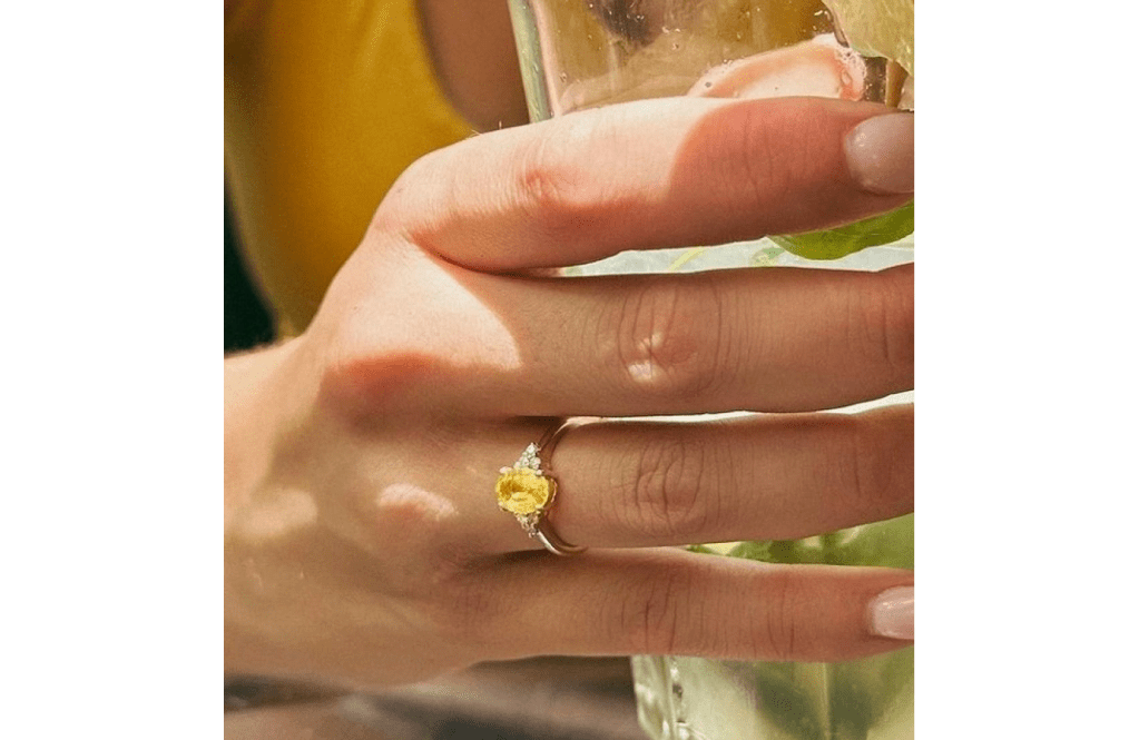 A woman 's hand with a ring on it and holding a glass of wine.