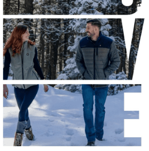 A couple walking in the snow with trees behind them.
