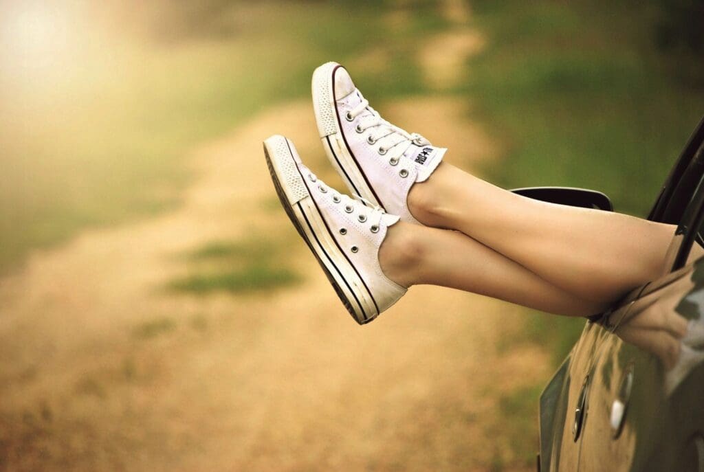 Legs in sneakers hanging from car.