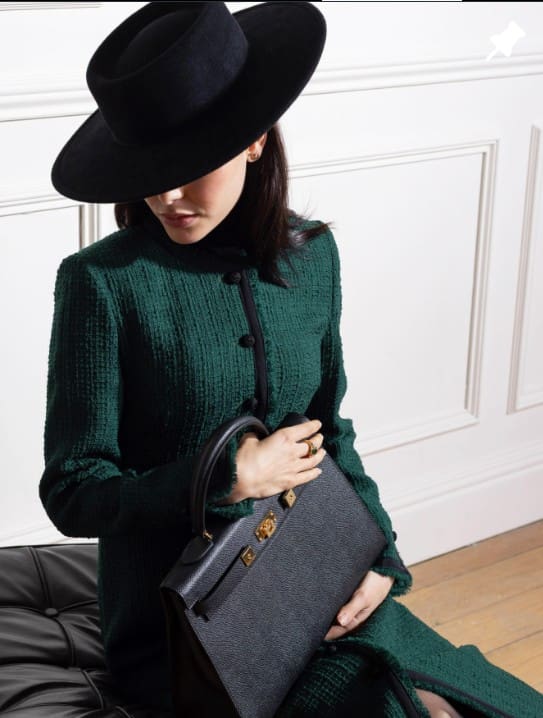 Woman wearing emerald coat, black hat, holding handbag